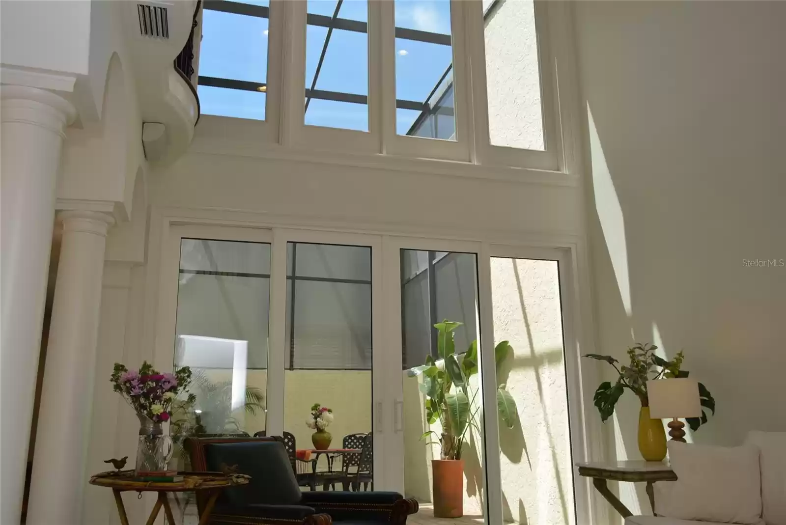 Living room, with 17’ ceilings, enjoys abundant natural light as a result of a floor-to-ceiling wall of glass overlooking two story, screened atrium